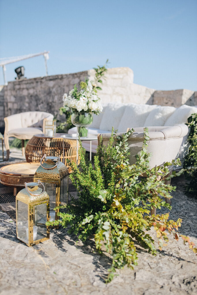 Reception setup at the rooftop of the Spanish Fortress with long banquet tables decorated in green and white florals, overlooking the sea.