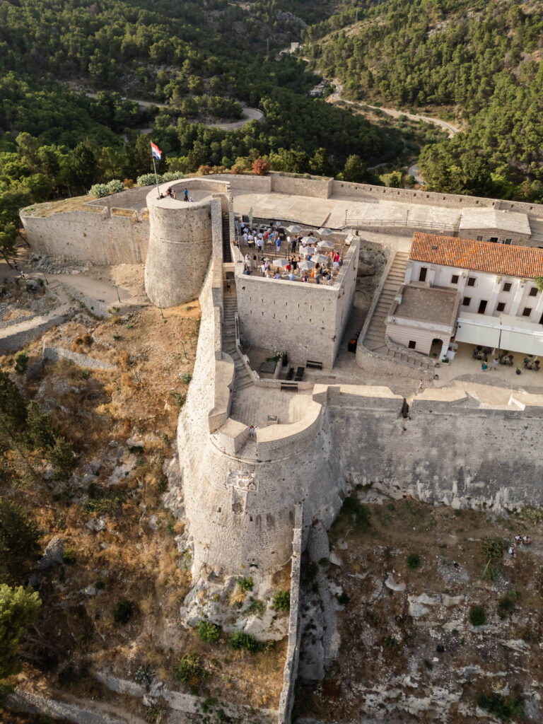 Aerial view of a historic fortress in Hvar set up for a wedding welcome party at sunset.