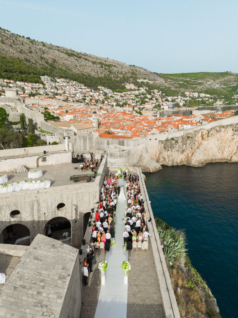 Morgan and Robbie’s three-day Dubrovnik wedding with a Hilton welcome dinner, Banje Beach party, and St. Lawrence Fortress ceremony, featuring signature cocktails, vintage bells, drummers, and a lively French band.