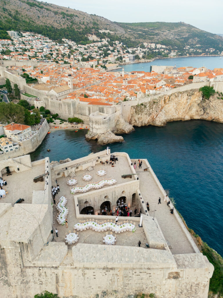 Morgan and Robbie’s three-day Dubrovnik wedding with a Hilton welcome dinner, Banje Beach party, and St. Lawrence Fortress ceremony, featuring signature cocktails, vintage bells, drummers, and a lively French band.